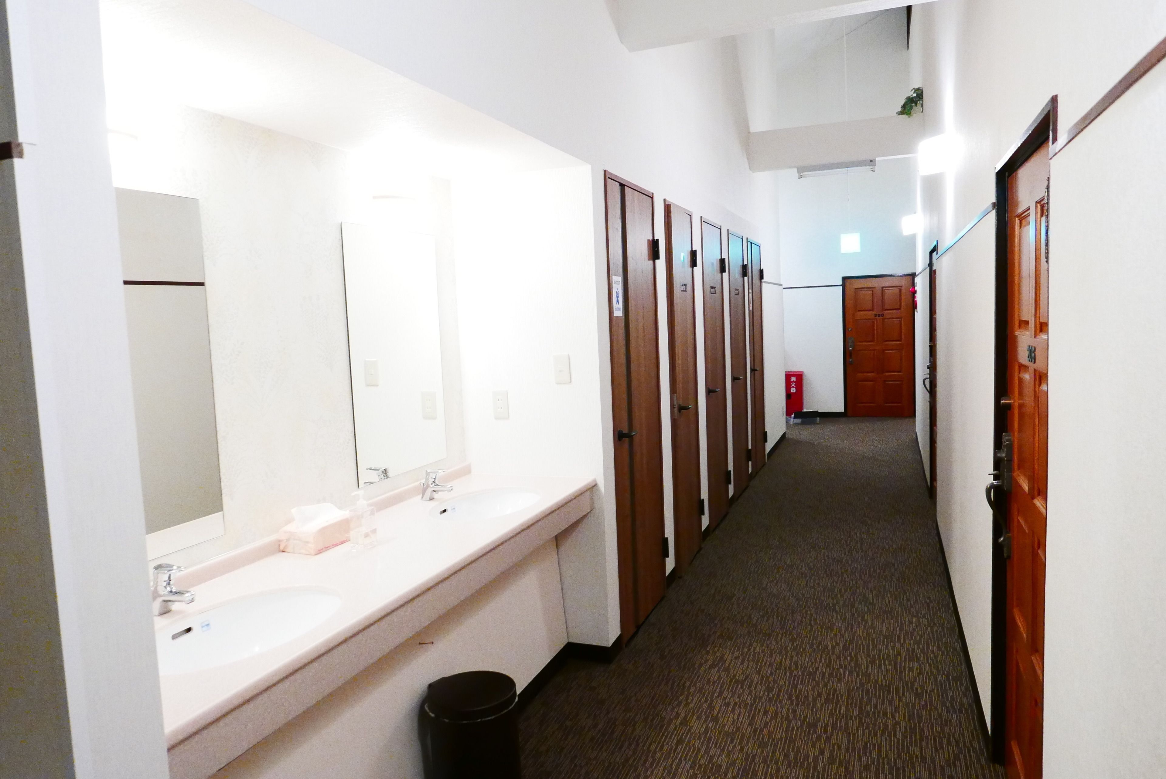 Un pasillo de hotel con un baño que incluye un lavamanos, espejo y taquillas de madera.