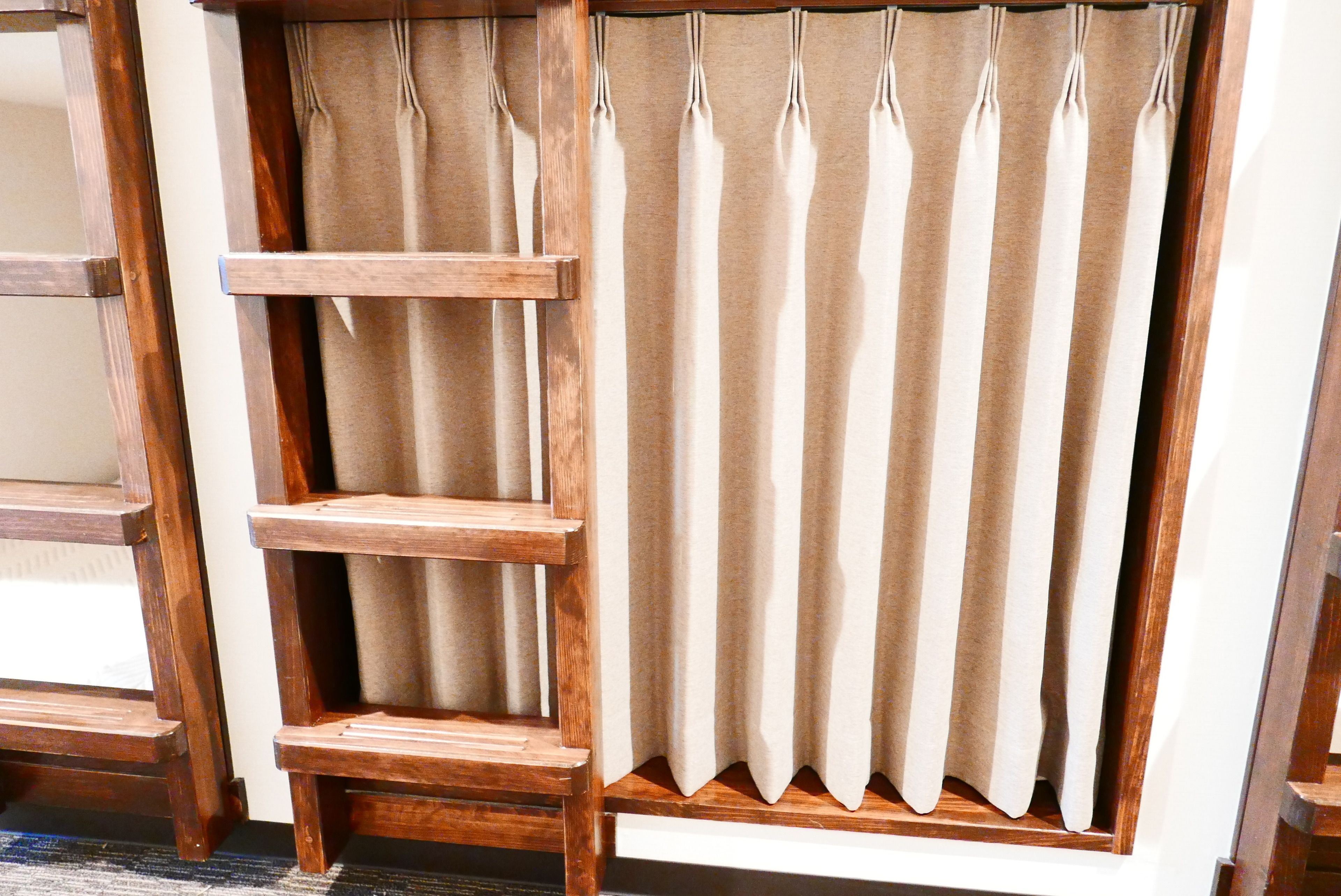 A wooden ladder shelf against a window with beige curtains.