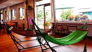 Une pièce avec deux hamacs, un plancher en bois, une grande fenêtre donnant sur l’extérieur et une plante en pot.