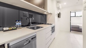 A modern kitchen with a dishwasher, sink, and stove. There is a window with a view of the outside. - Whitehorse Apartment Hotel (Mont Albert)