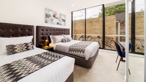 A modern hotel room with two beds, a large window, and a view of the outside. - Whitehorse Apartment Hotel (Mont Albert)