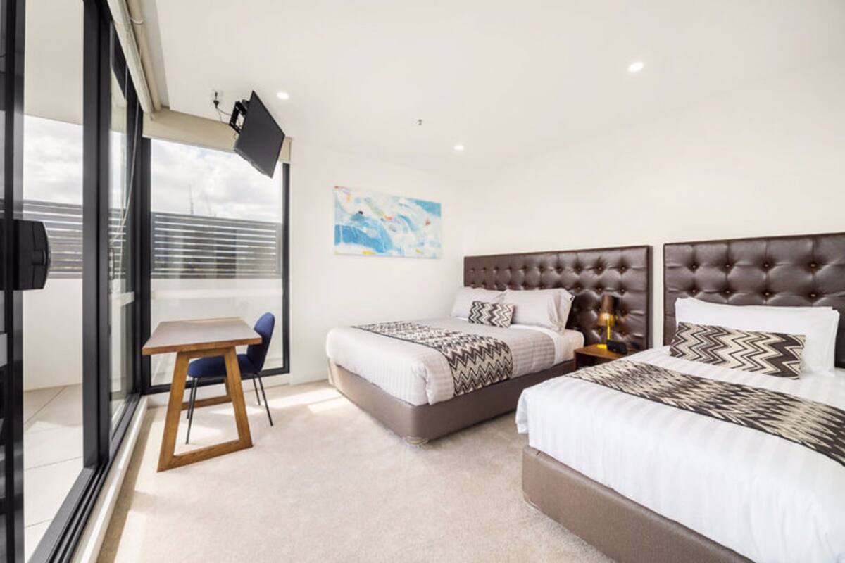 A modern hotel room with two beds, a desk, and a chair.