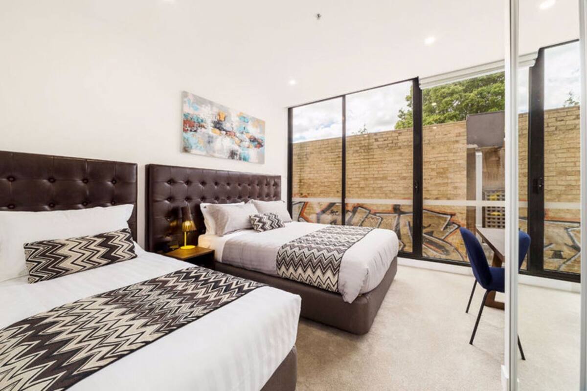 A hotel room with two beds, a large window, and a balcony.