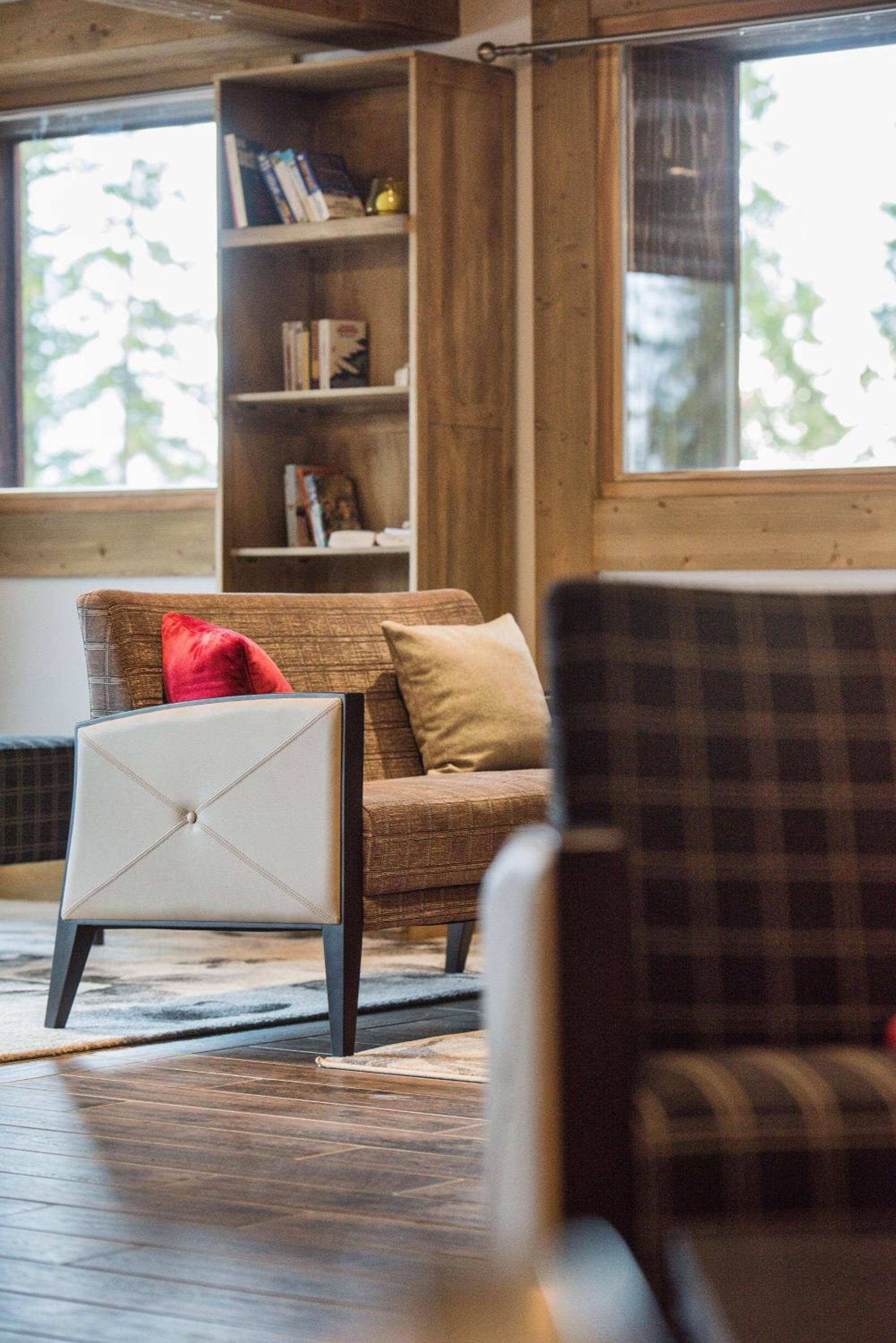 Ein gemütliches Zimmer mit Holzboden, einer Couch mit Kissen, einem Sessel und einem Bücherregal voller Bücher und Dekoration.