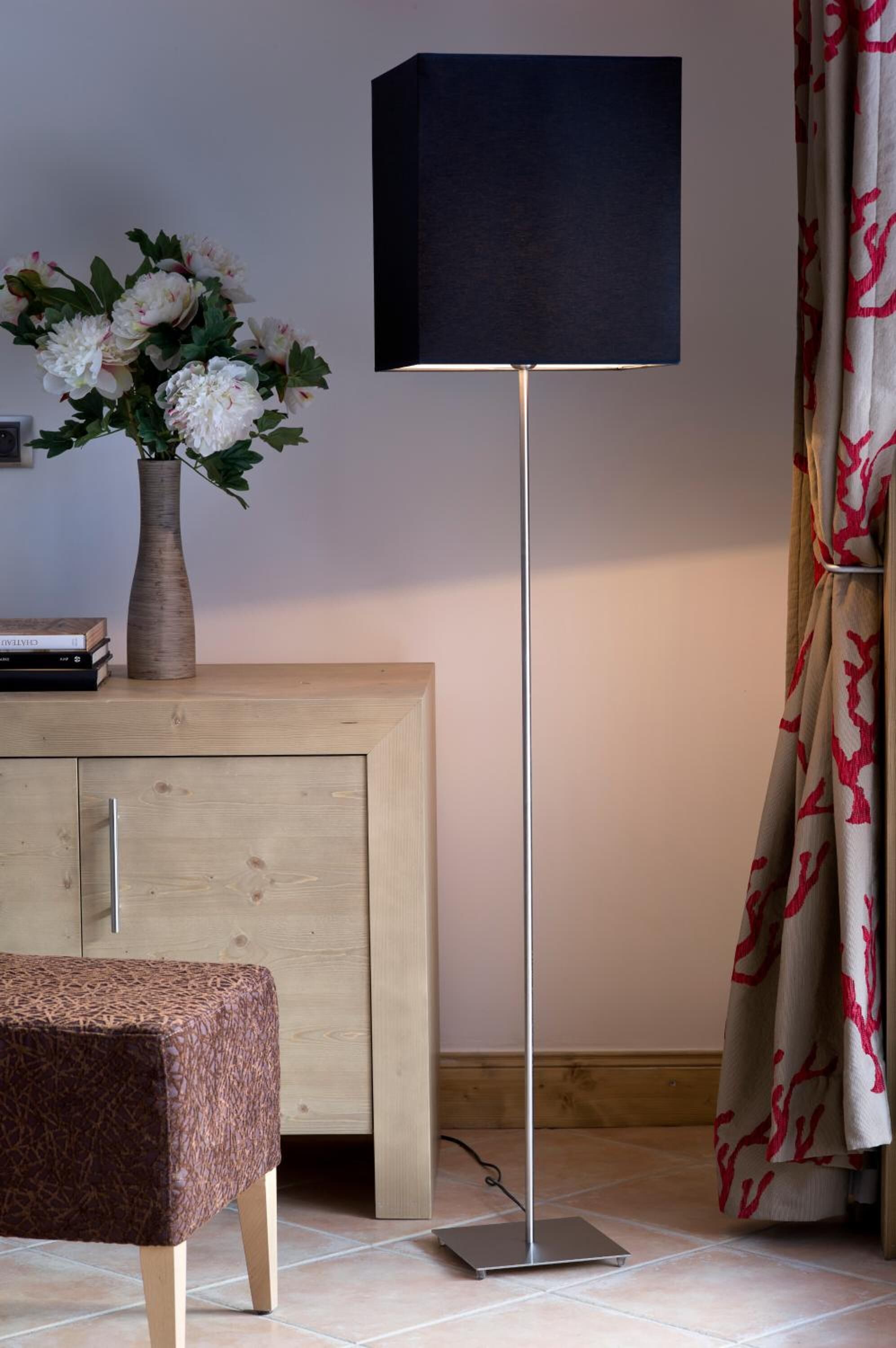 A modern room with a wooden cabinet, a floor lamp, a small table, and a curtain with a red pattern.