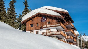Um chalé de madeira com uma placa indicando "CGH Residence Hotel Spa & Wellness" na fachada, rodeado por encostas e árvores cobertas de neve.