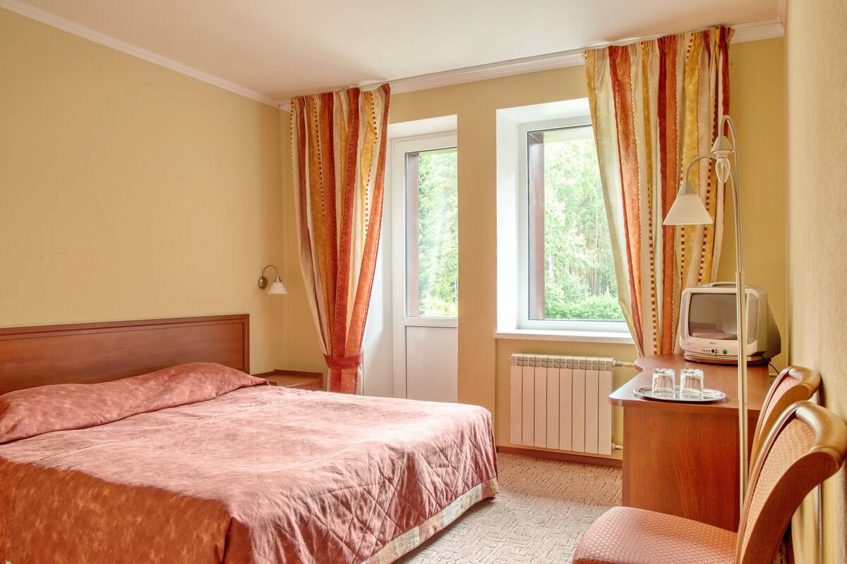 A hotel room with a bed, a desk with a television, and curtains.