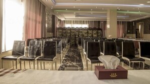 Een vergaderzaal met rijen stoelen, een marmeren vloer en een tafel met zakdoekjes.
