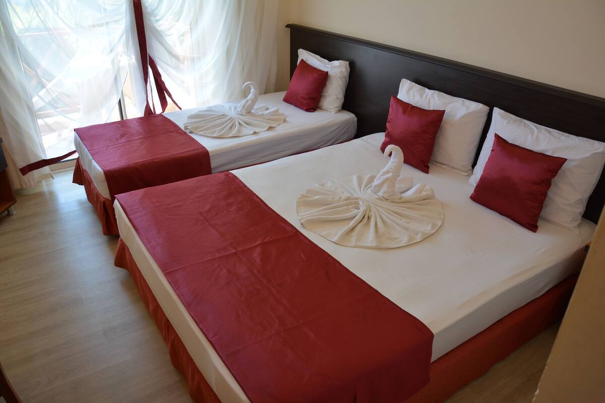 Dos camas dobles con ropa de cama roja y blanca, un cabecero de madera y piso de madera.