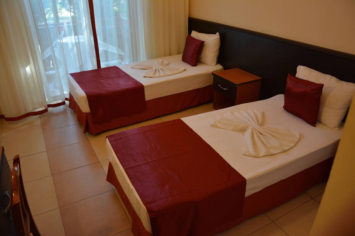 Dos camas individuales con cubrecamas rojos, sábanas blancas y una almohada roja en cada cama.