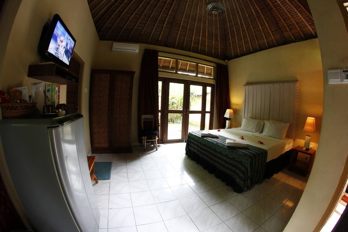 A hotel room with a bed, a television, a refrigerator, a window, and a door.