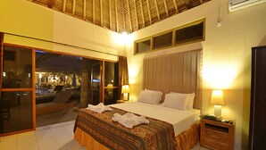 Une chambre d’hôtel avec un grand lit, deux lampes de chevet, une table de chevet en bois et une porte-fenêtre coulissante donnant sur un espace extérieur.
