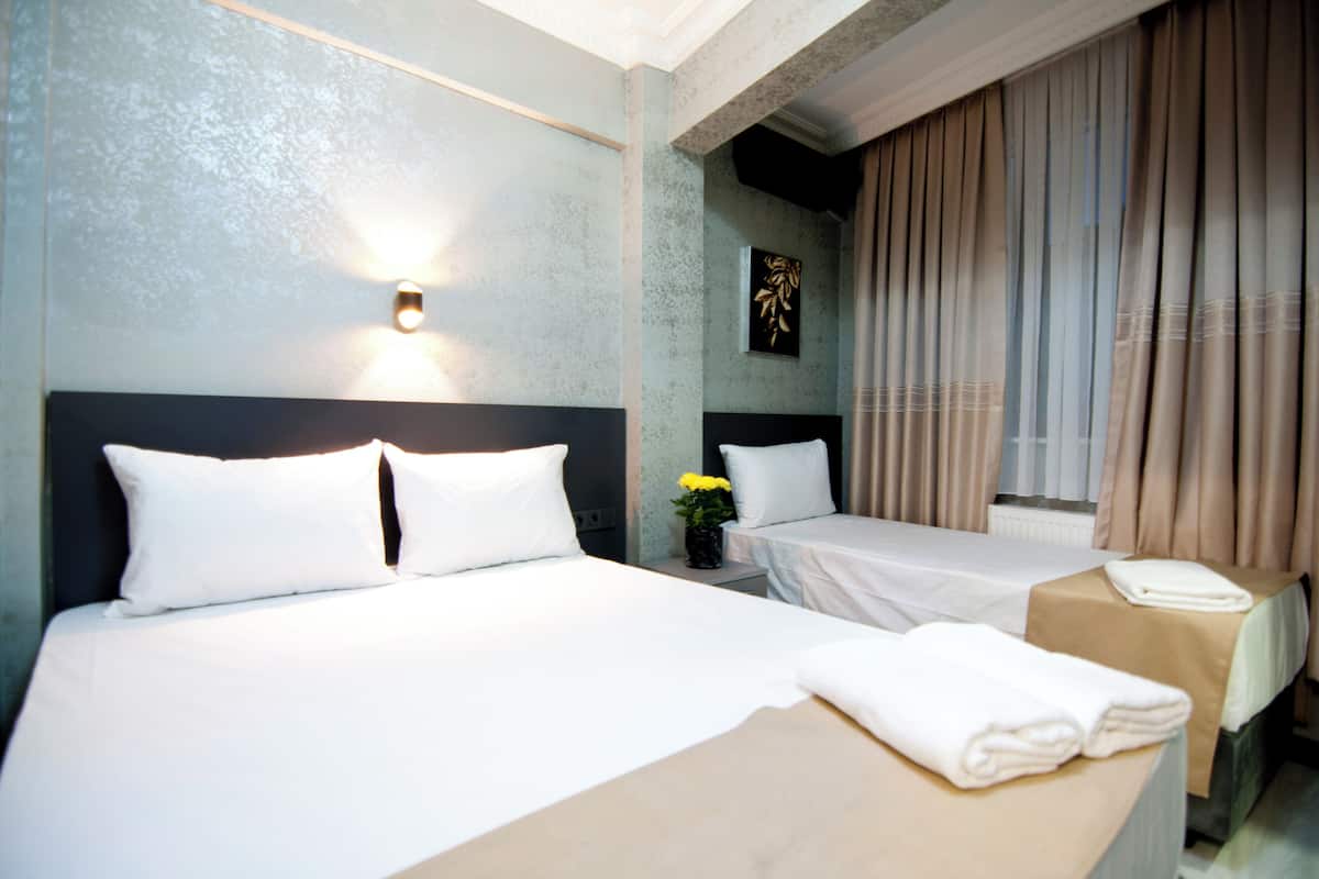 Une chambre d’hôtel avec deux lits, une table de chevet ornée d’un vase de fleurs et une lampe fixée au mur.