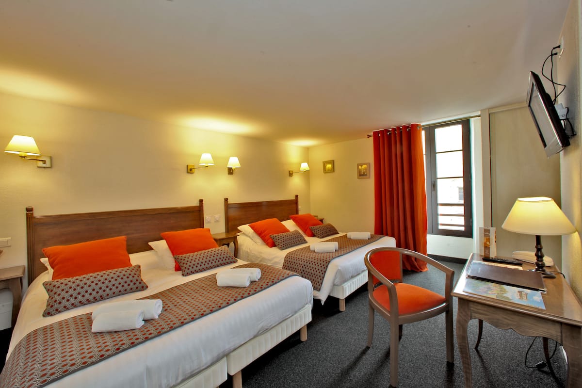 Habitación de hotel con dos camas, un escritorio, una silla y televisión en la pared.