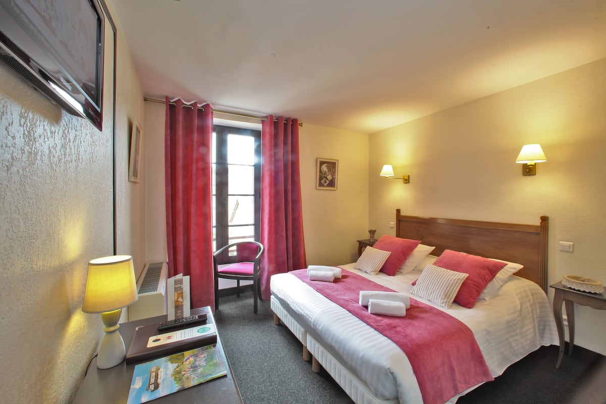 Una habitación de hotel con dos camas, un escritorio con lámpara, una silla y una mesita con un pastel.