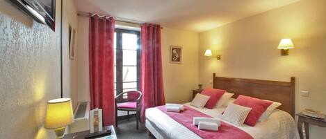 A hotel room with two beds, a desk with a lamp, a chair, and a small table with a cake.