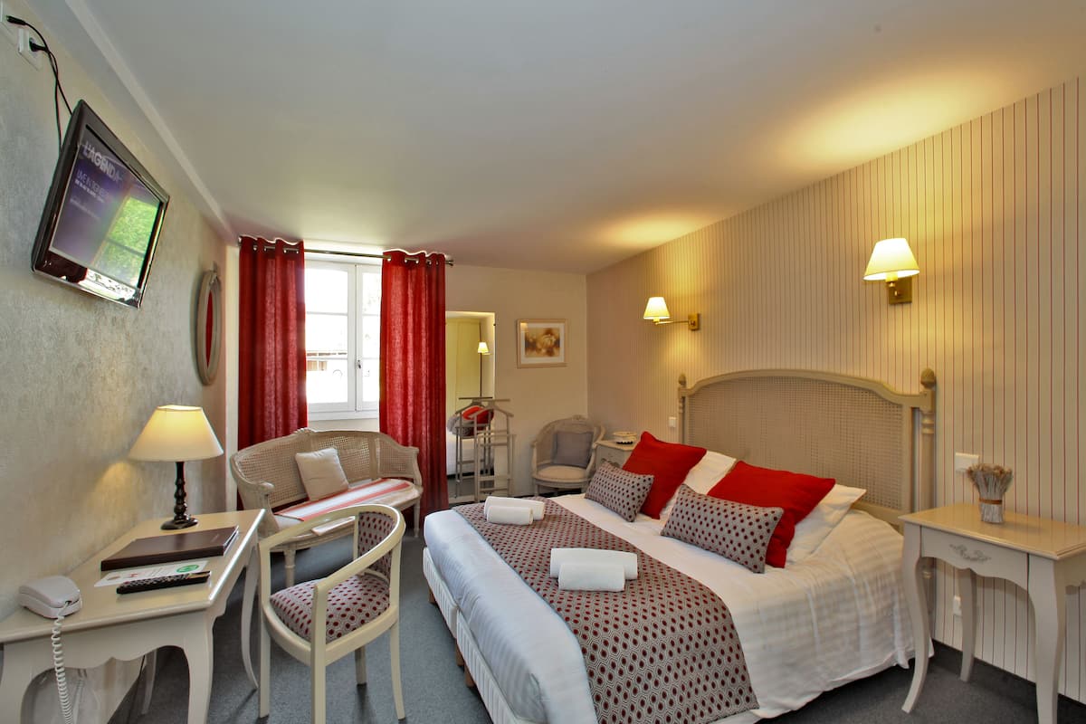 Habitación de hotel con cama, escritorio con teléfono, silla, televisor y mesita de noche con lámpara.
