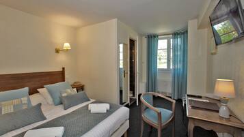 Une chambre d’hôtel avec un lit, une chaise, un bureau, une télévision et une fenêtre avec des rideaux.