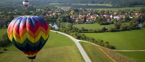 A hot air balloon over a rural landscape with a winding road and a village in the background.