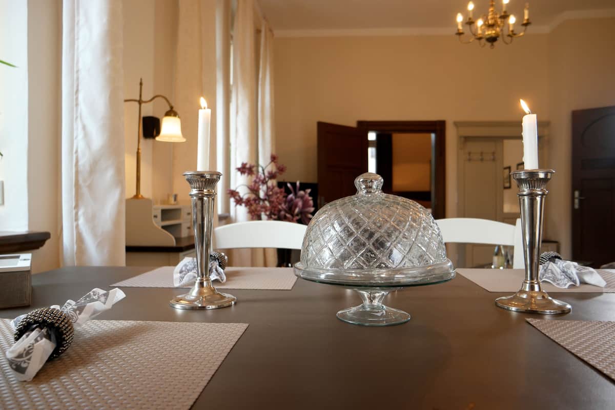 Une table à manger agrémentée d’un centre de table en forme de dôme de verre, de deux bougies allumées et d’un vase rempli de fleurs violettes.