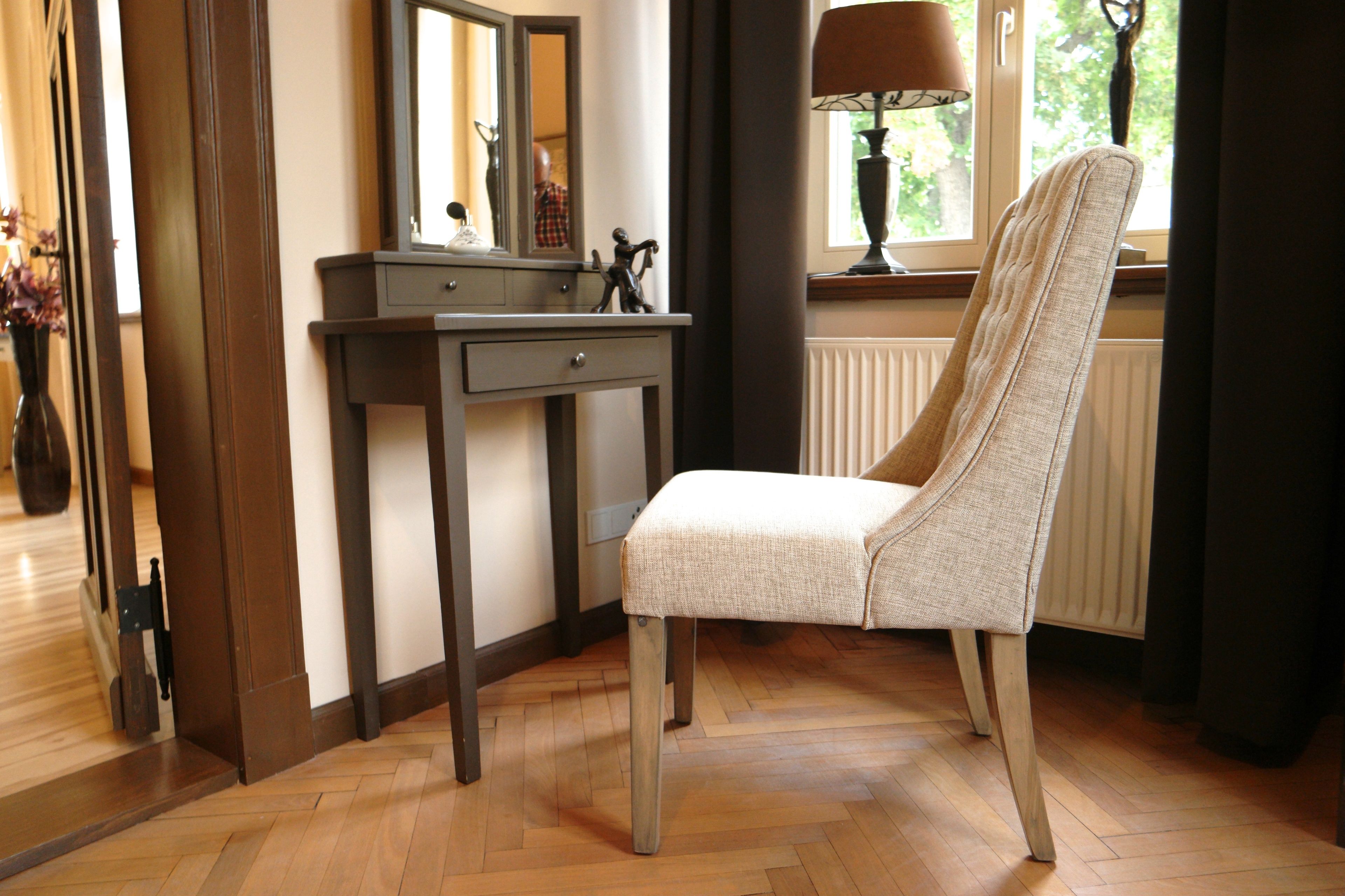 Una silla con asiento y respaldo acolchados, ubicada junto a un aparador de madera con un espejo y una pequeña estatua encima.