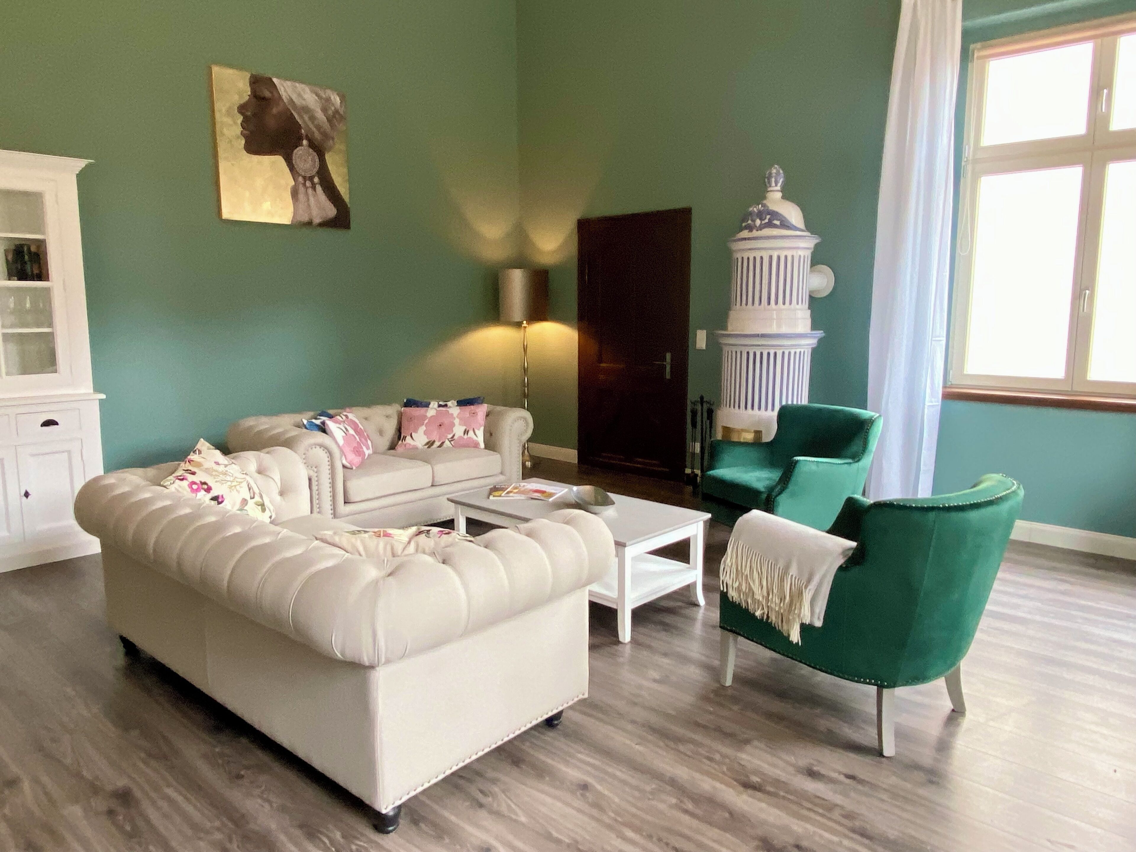 A living room with a sofa, a coffee table, a green armchair, a white cabinet, and a wall-mounted lamp.