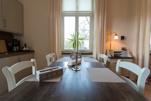 Un coin repas avec une table en bois, des chaises blanches, une machine à café et une fenêtre avec des rideaux.