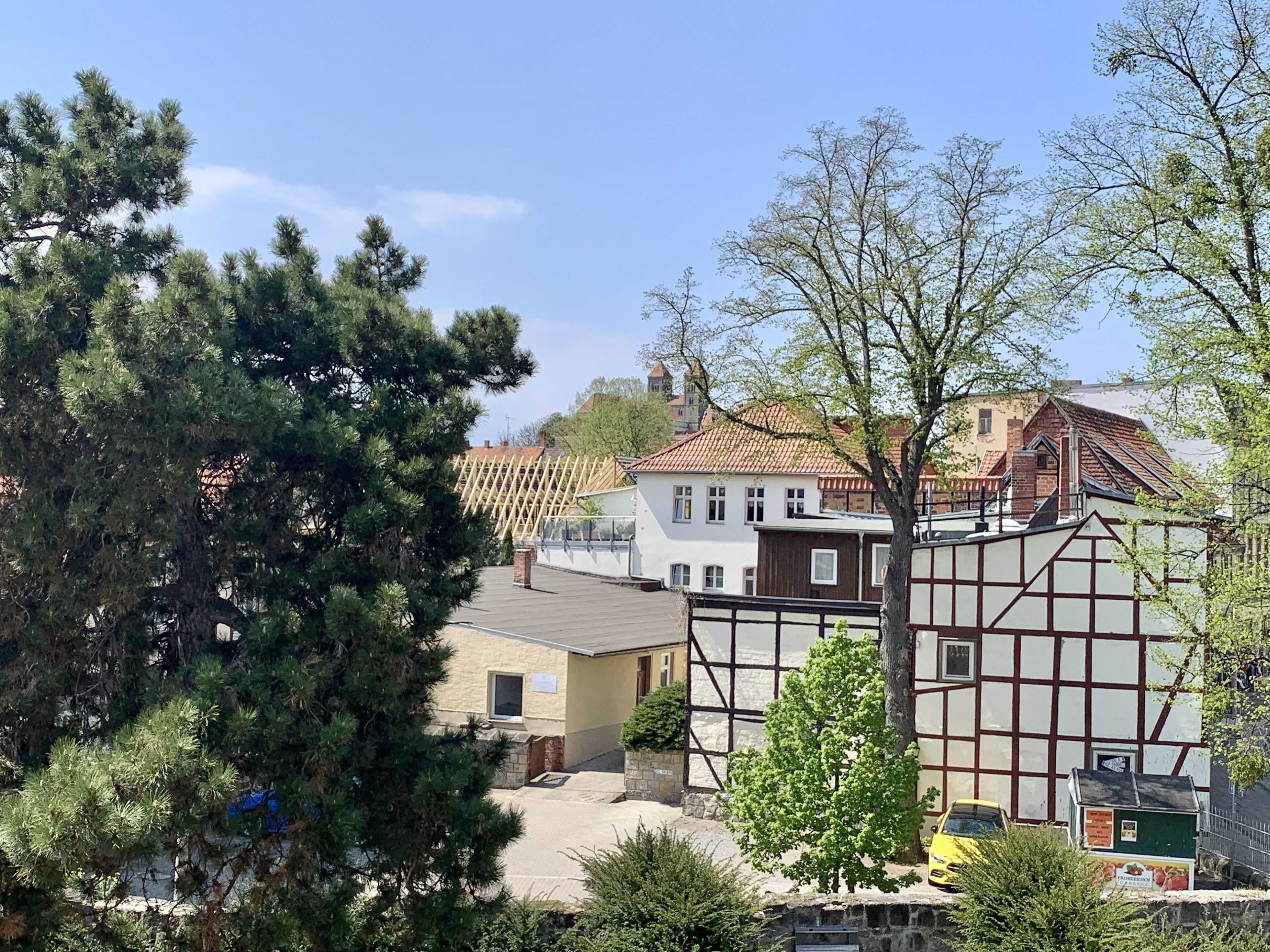 Un pueblo europeo tradicional con casas de entramado de madera, un cielo azul despejado y diversos árboles.