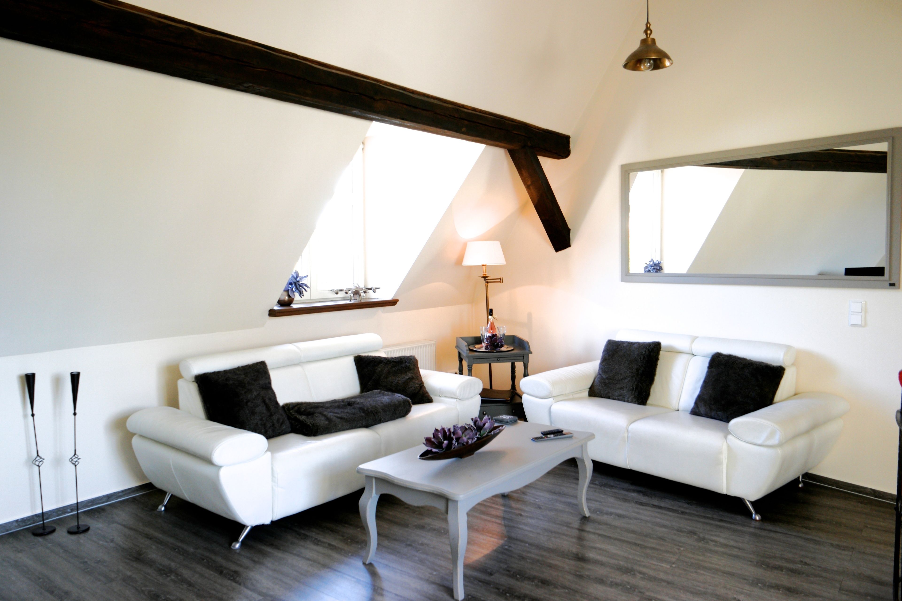 A modern living room with two white sofas, a coffee table, a lamp, and a large mirror on the wall.