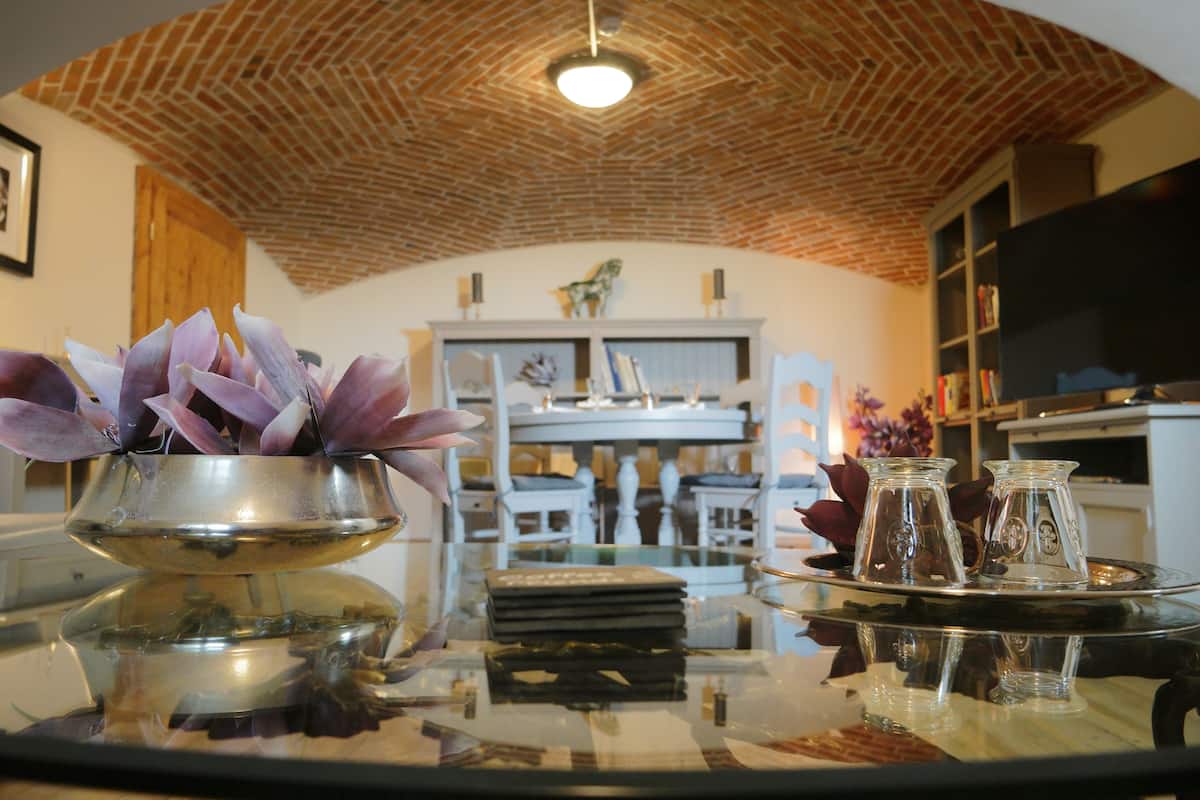 Une pièce avec un plafond en briques, une table en verre ornée d’un vase de fleurs violettes et une étagère sur laquelle sont disposés des objets décoratifs.