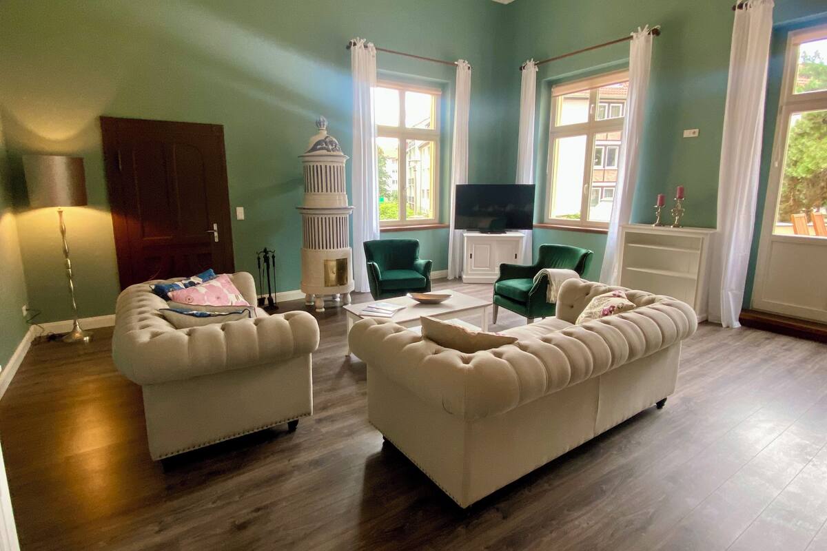 Un salon avec deux canapés blancs, un parquet, une cheminée blanche et un téléviseur.