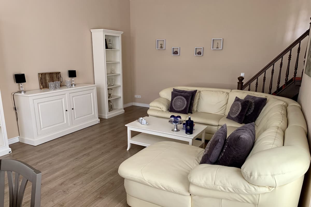Un salon avec un canapé en cuir beige, un buffet blanc et un escalier.