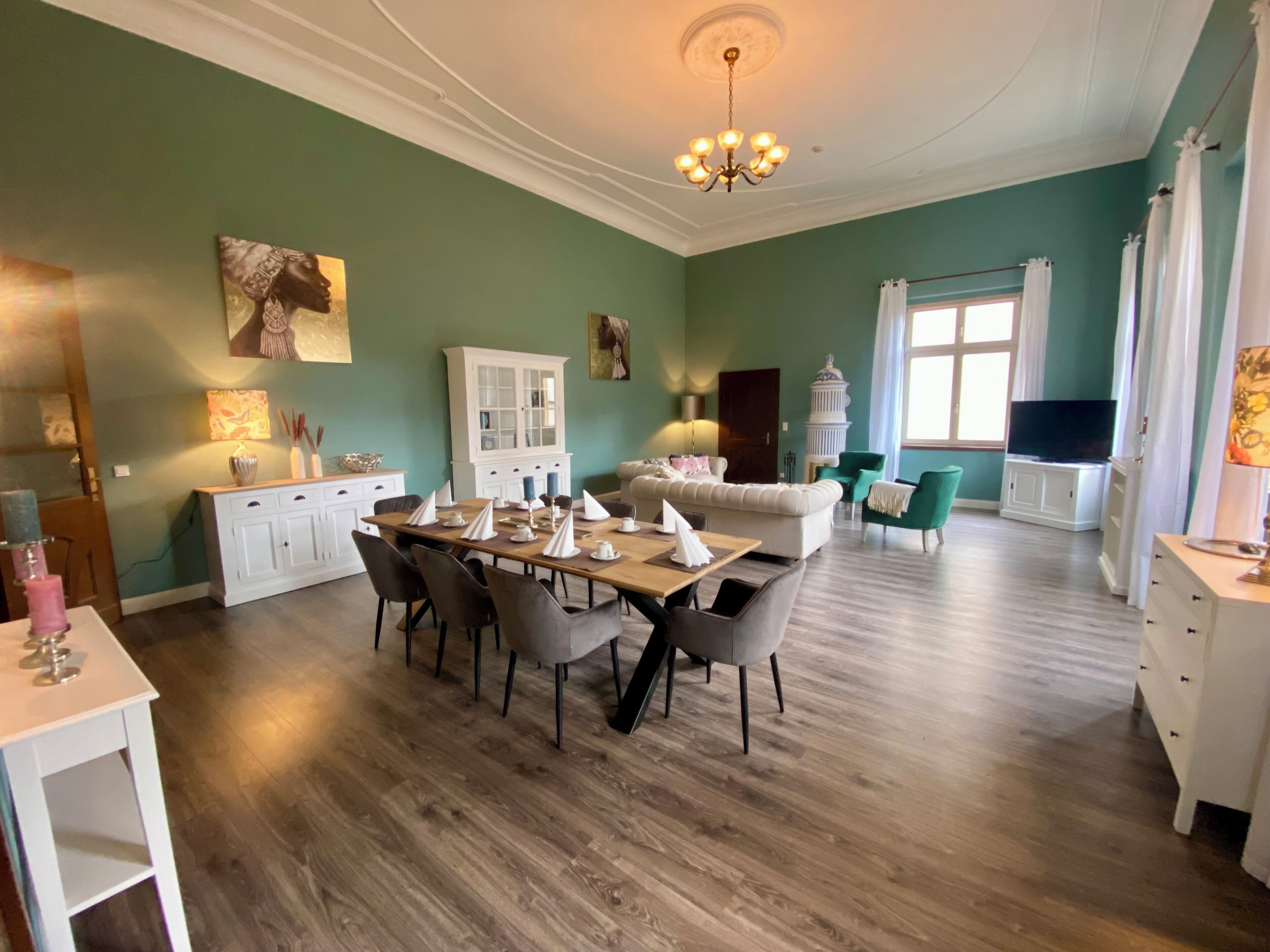 A spacious living room with a dining area, a white cabinet, a chandelier, and a television.