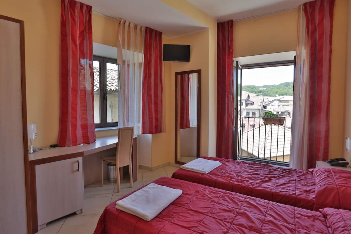 A hotel room with two beds, a desk, a chair, and a large window with curtains.
