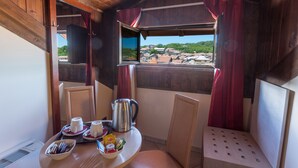 A cozy cabin with a dining area featuring a table set with cups, a kettle, and a plate of food. A window offers a view of a village. - Hotel Conte Ruggero (Serra San Bruno)