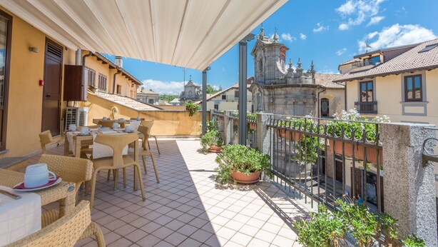A terrace with wicker furniture, potted plants, and a view of historic buildings. - Hotel Conte Ruggero (Serra San Bruno)