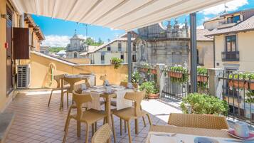 Eine Terrasse mit Korbmöbeln, Fliesenboden und Blick auf Gebäude im Hintergrund.