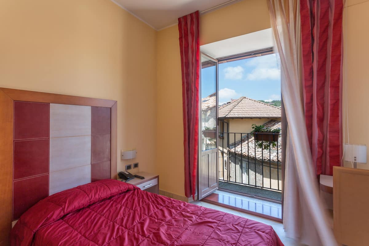 A hotel room with a bed, a nightstand, a phone, and a view of a balcony with a railing.