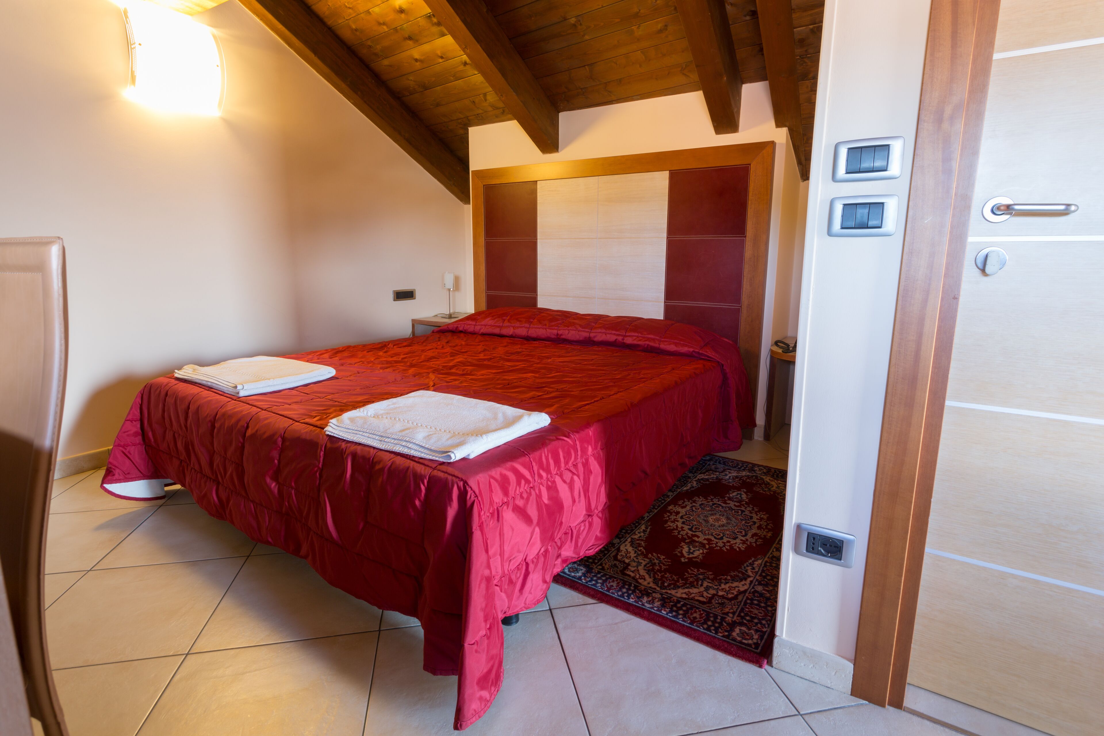 A bedroom with a bed, a bedside table, a nightstand, a wall-mounted light, and a door with a handle.