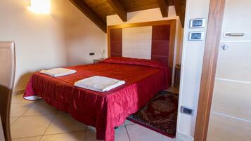A bedroom with a bed, a bedside table, a nightstand, a wall-mounted light, and a door with a handle.