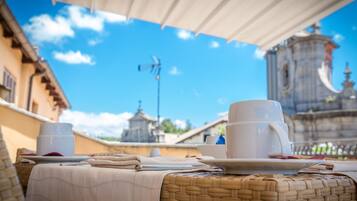 A table set with white cups and saucers, a folded napkin, and a menu on a wicker table under a white canopy.
