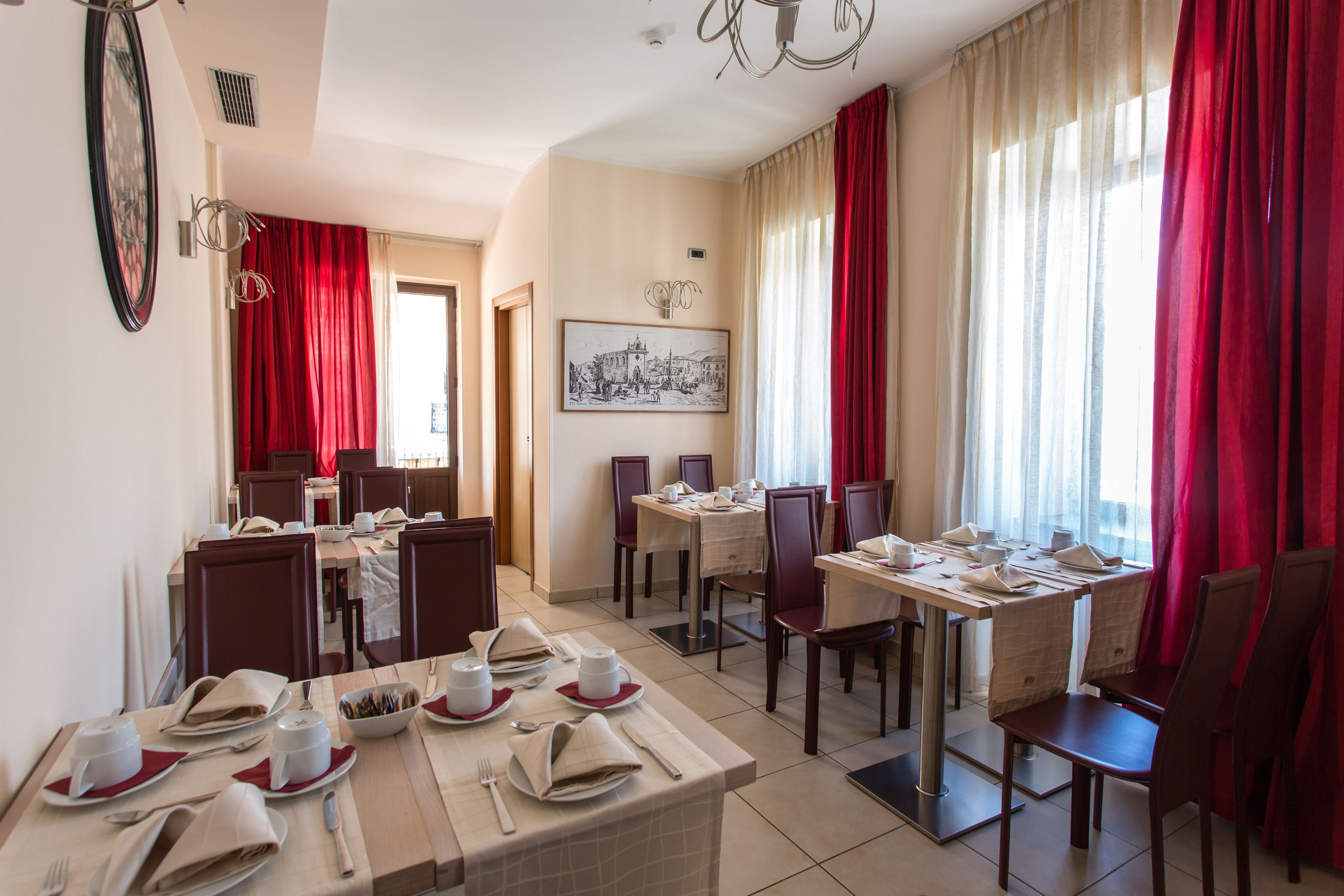 Een restaurantruimte in een hotel met gedekte tafels, rode gordijnen en een ingelijst schilderij aan de muur.