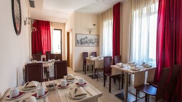 Un comedor de hotel con mesas dispuestas para comer, cortinas rojas y un cuadro en la pared.
