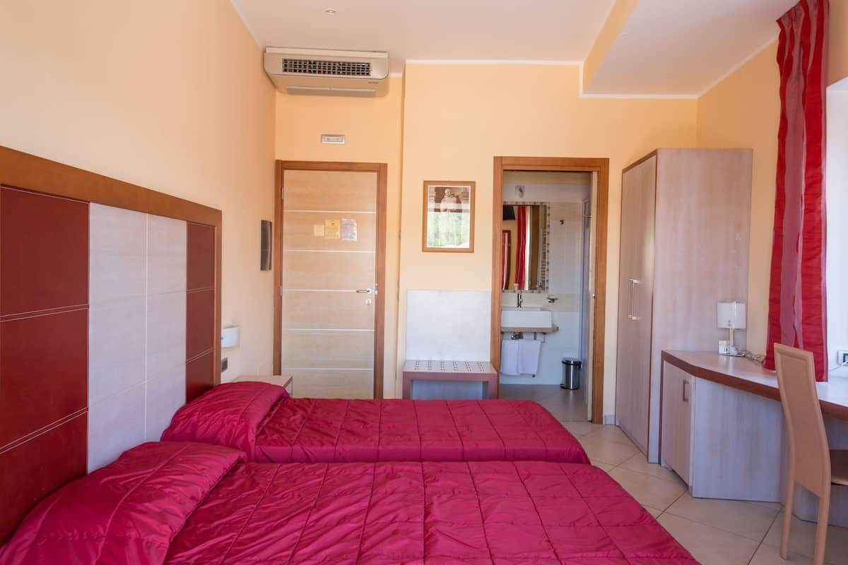 A bedroom with two beds, a desk, a chair, a mirror, and a bathroom visible through an open door.