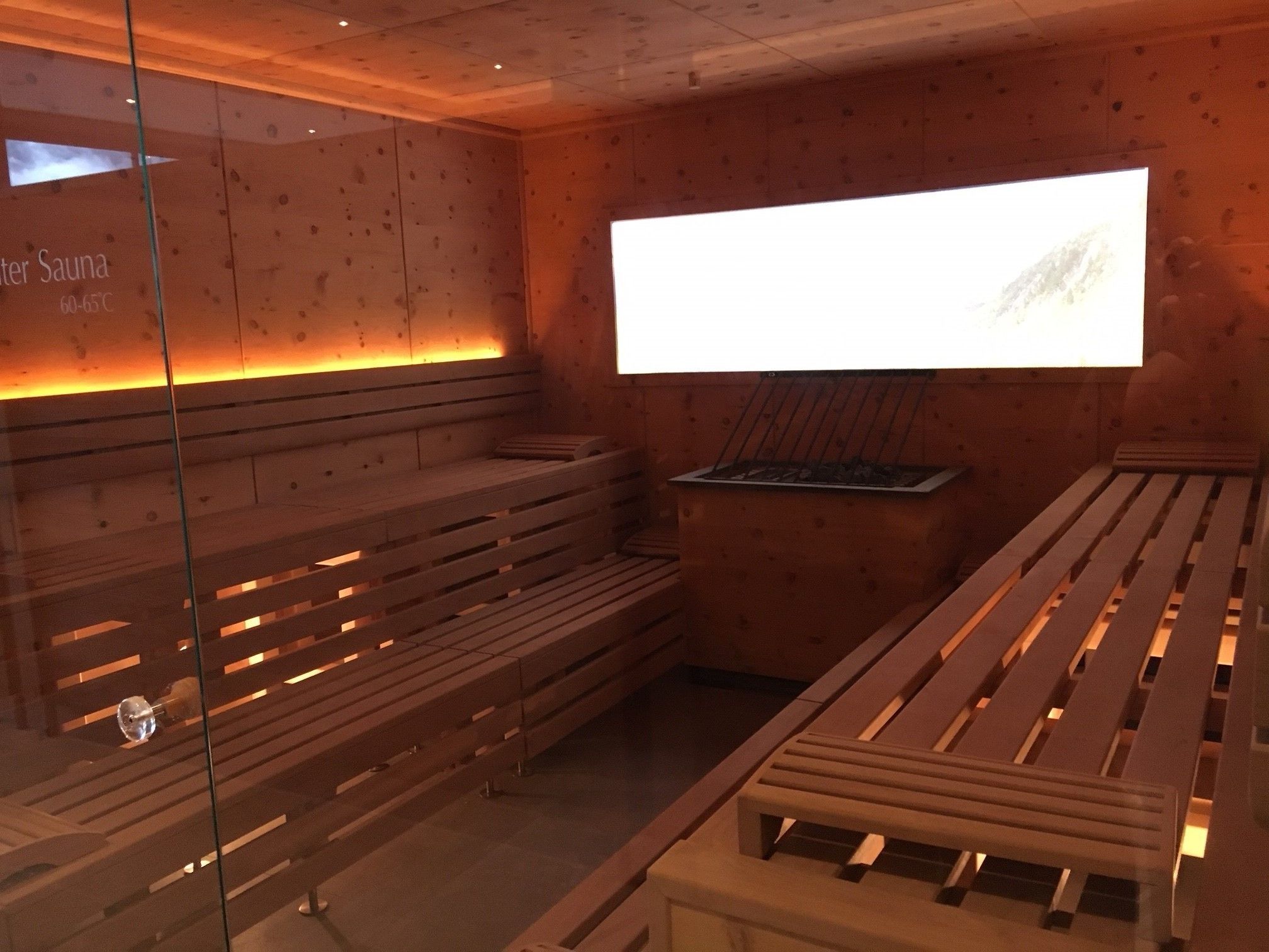 A sauna room with wooden benches and a wall-mounted sauna heater.