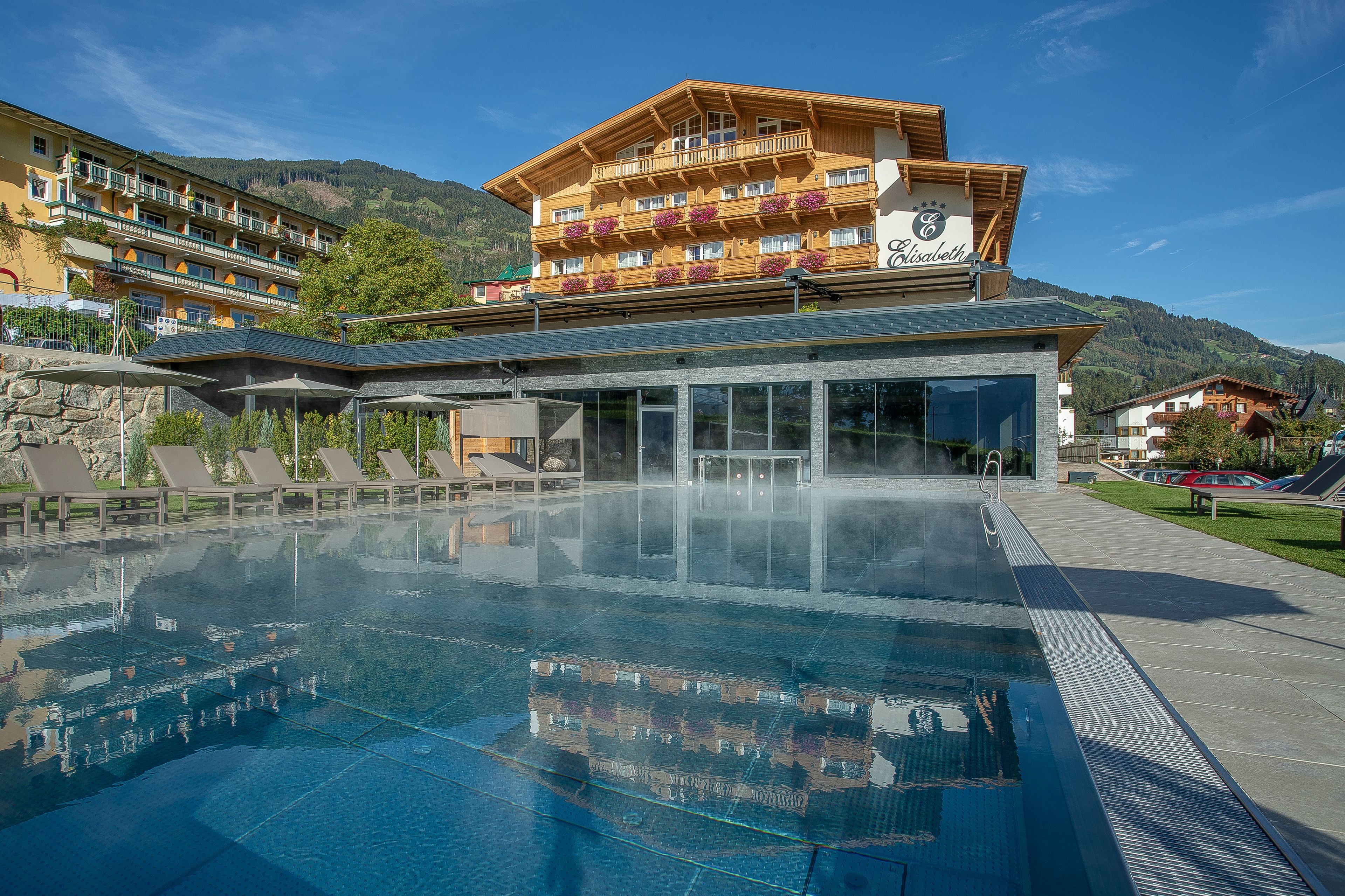 Ett hotell med en stor utomhuspool, träterrasser och utsikt över bergen.