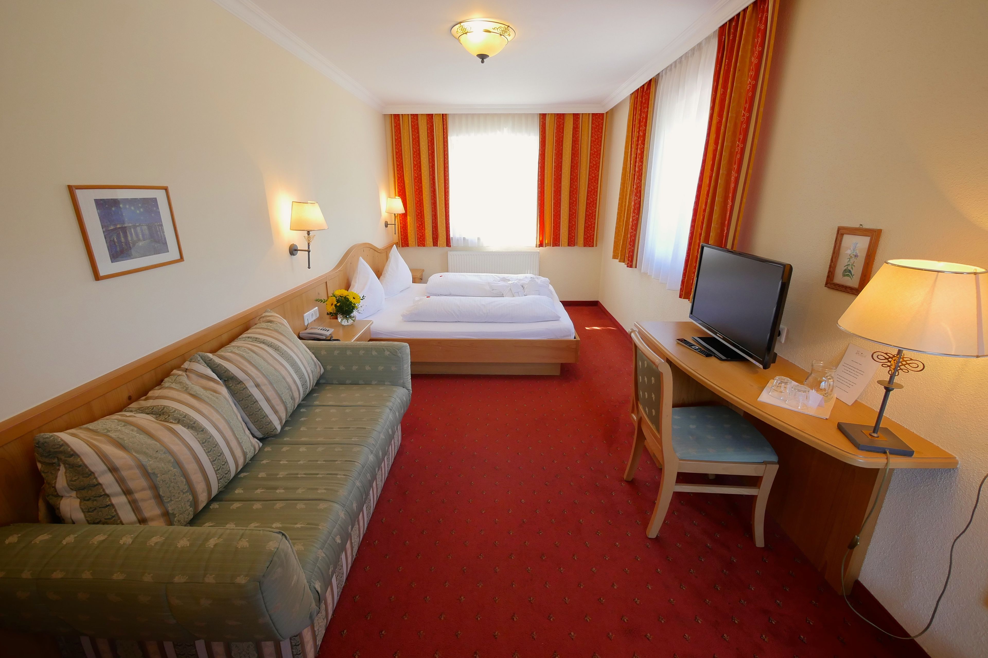 A hotel room with a bed, a sofa, a desk with a computer, and a TV.