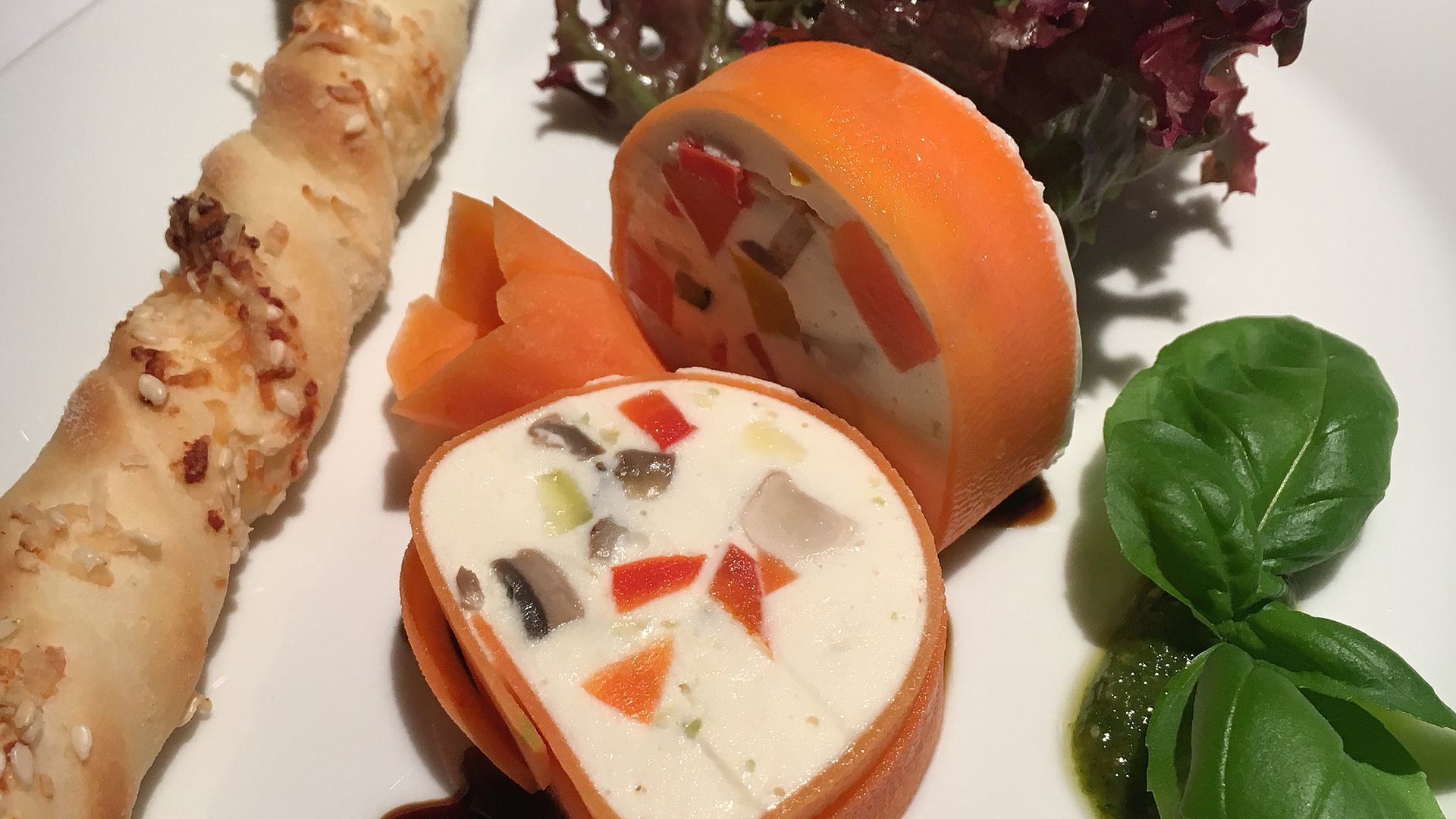 A plate with a rolled pastry, a sliced orange, and a bowl of soup with vegetables.