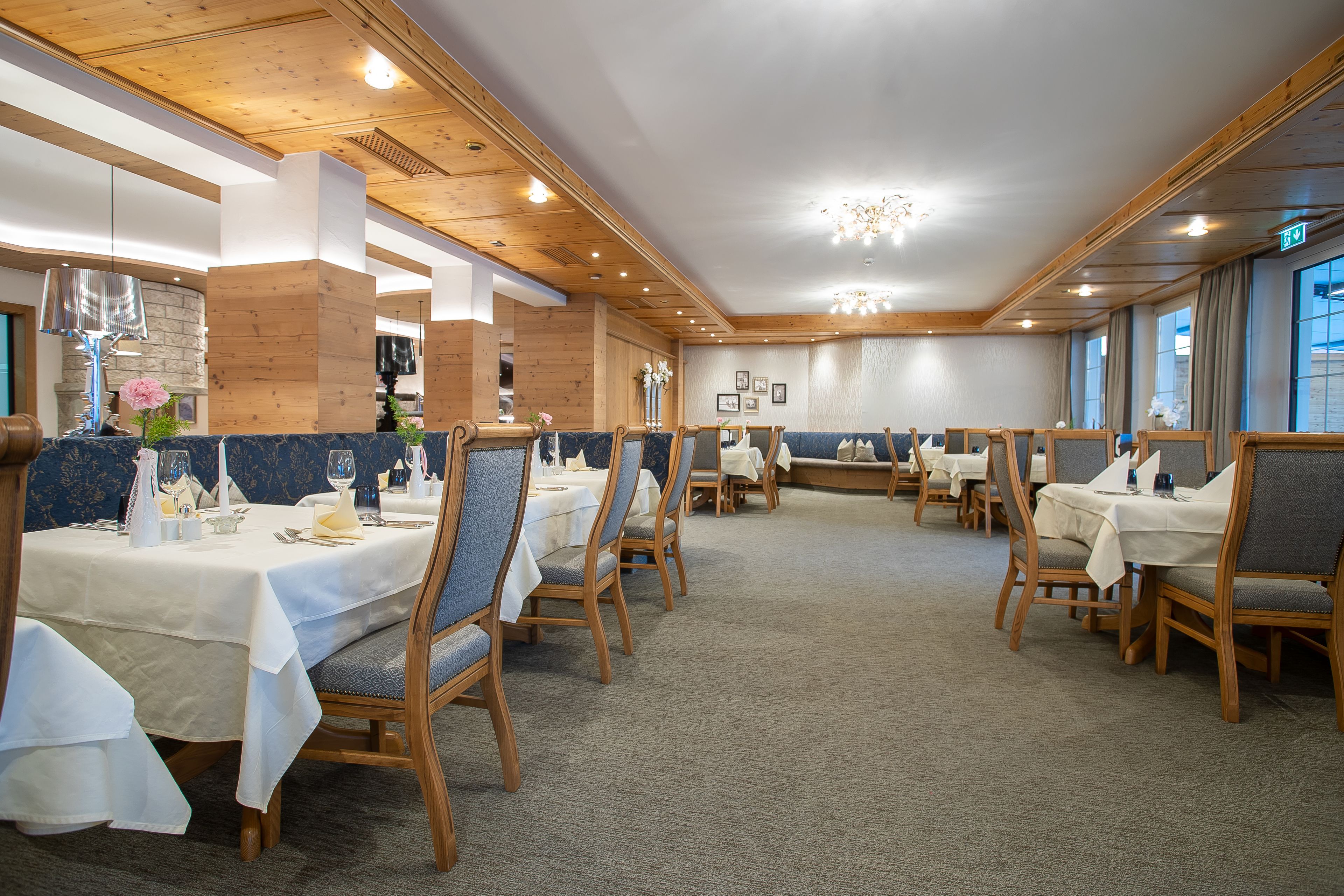 A restaurant with wooden ceiling beams, tables set with white tablecloths, and blue cushioned chairs.