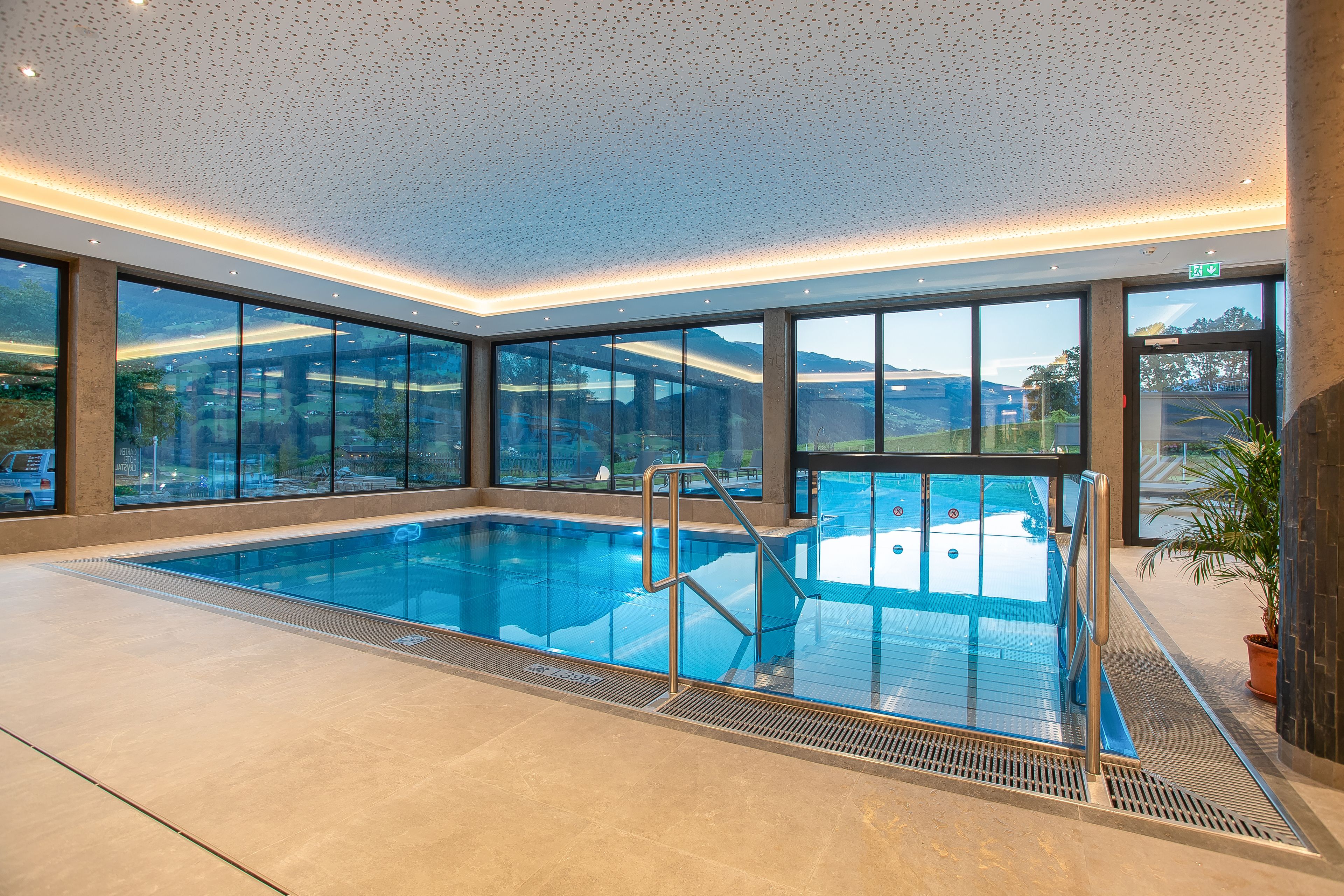 Une piscine intérieure avec des parois en verre transparent, un escalier en métal et une vue sur le paysage extérieur.